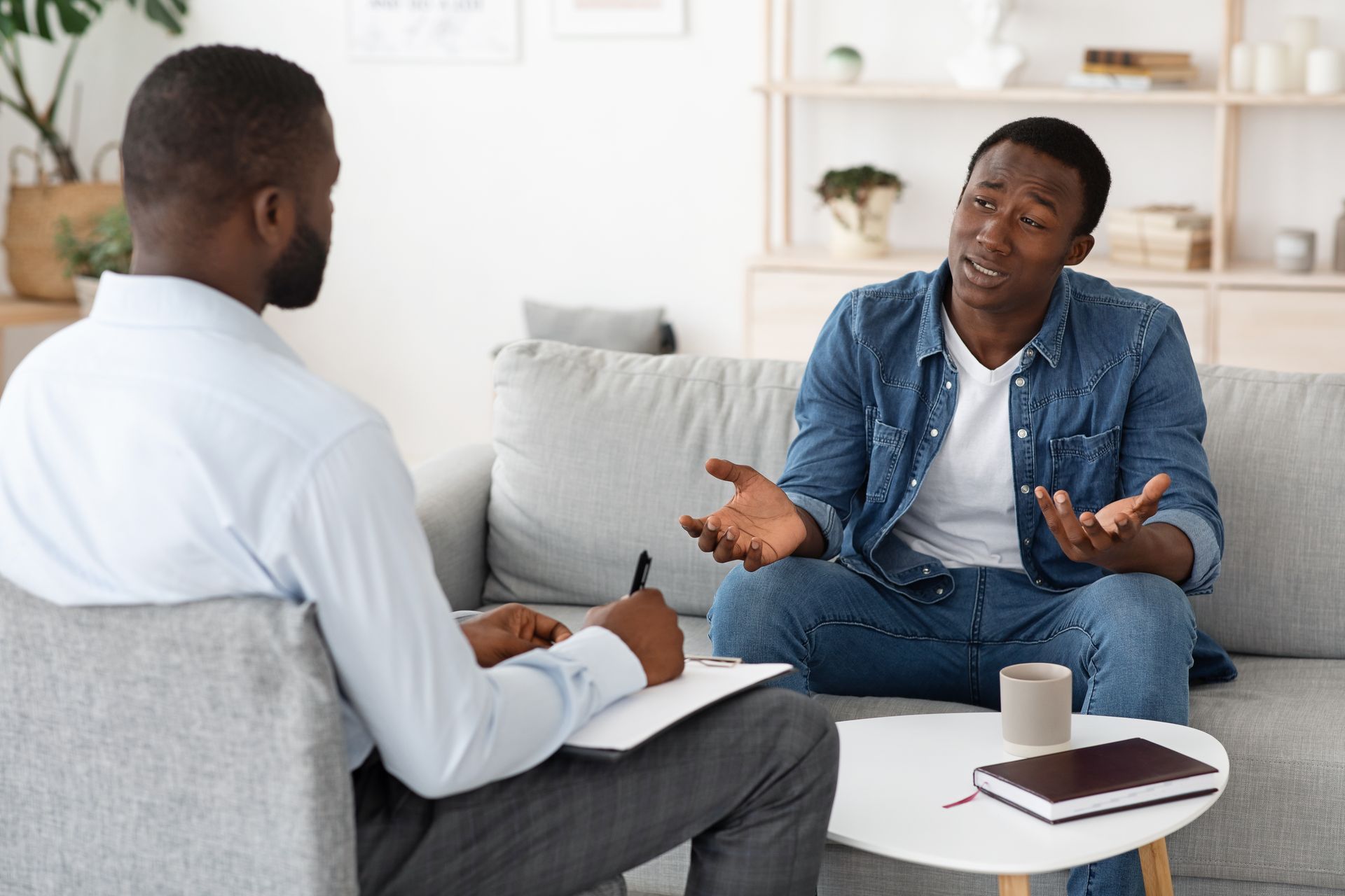 A man on a sofa talking openly with a therapist who listens and takes notes